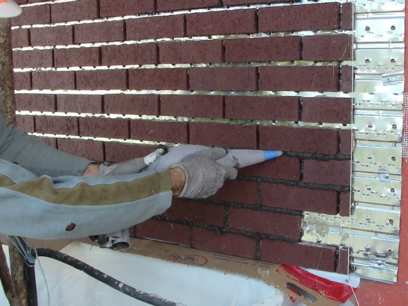 worker installing mortar between thin bricks on a thin brick metal panel